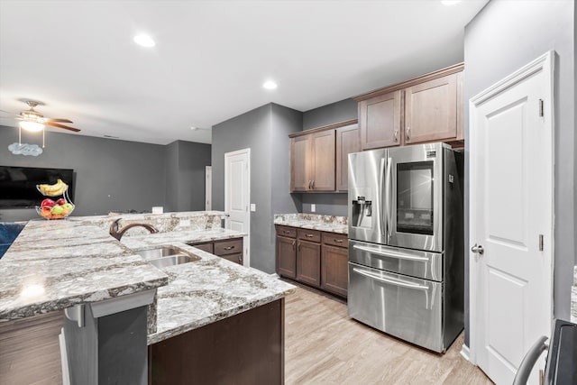 kitchen featuring light stone counters, stainless steel fridge with ice dispenser, ceiling fan, a sink, and light wood-style floors