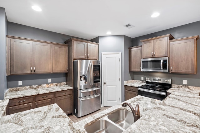 kitchen featuring visible vents, a sink, light stone counters, recessed lighting, and stainless steel appliances