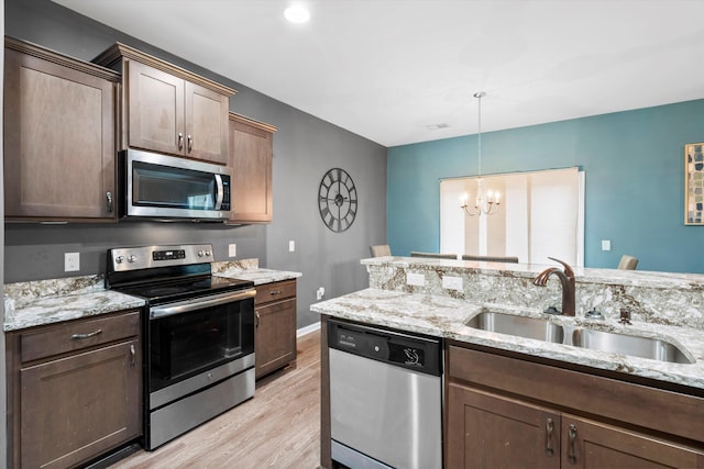 kitchen featuring light stone counters, a sink, appliances with stainless steel finishes, a notable chandelier, and light wood-type flooring