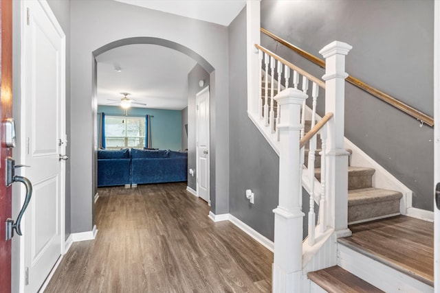 foyer featuring baseboards, arched walkways, wood finished floors, and a ceiling fan