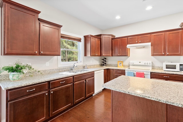 kitchen featuring white appliances, light stone counters, dark wood-style flooring, under cabinet range hood, and a sink