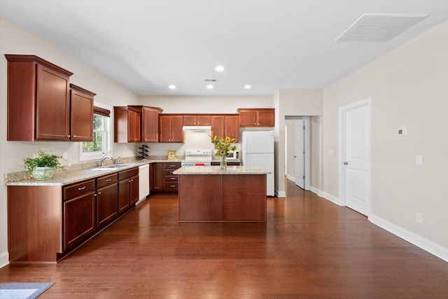 kitchen with dark wood-style flooring, visible vents, a sink, white appliances, and under cabinet range hood