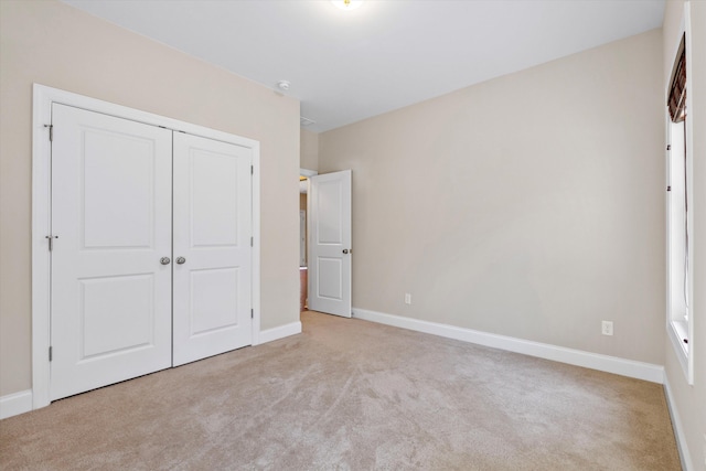 unfurnished bedroom featuring light carpet, a closet, and baseboards