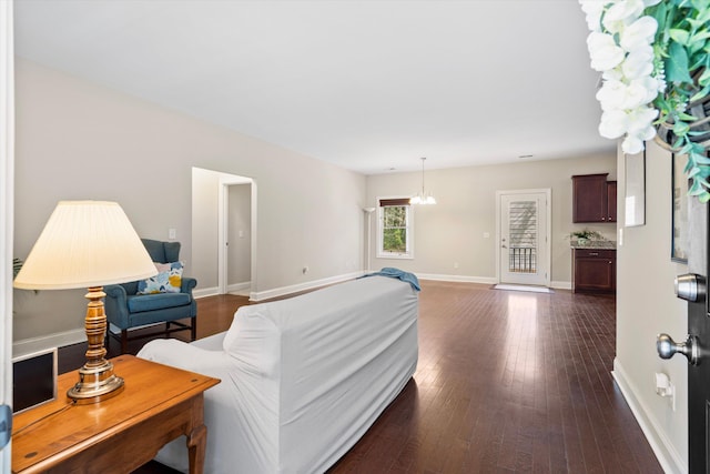 living area featuring dark wood-style floors, a notable chandelier, and baseboards