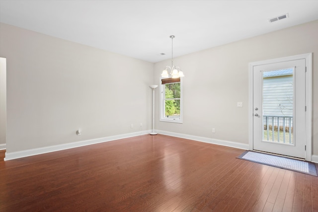 spare room with dark wood-style flooring, visible vents, a notable chandelier, and baseboards