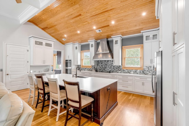 kitchen with a center island with sink, wood ceiling, wall chimney range hood, and light wood-type flooring