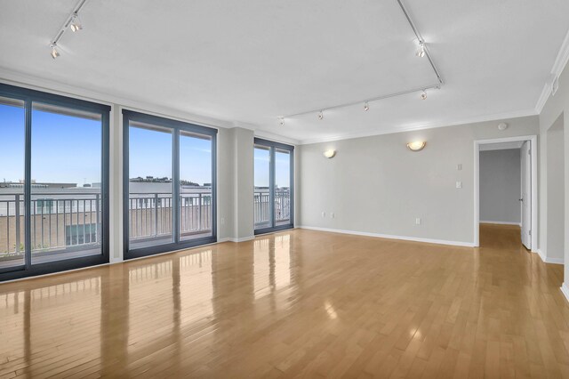 empty room with a wall of windows, track lighting, wood-type flooring, and ornamental molding