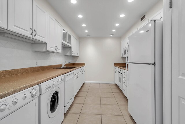 interior space featuring light tile patterned flooring, white appliances, white cabinets, washing machine and clothes dryer, and sink