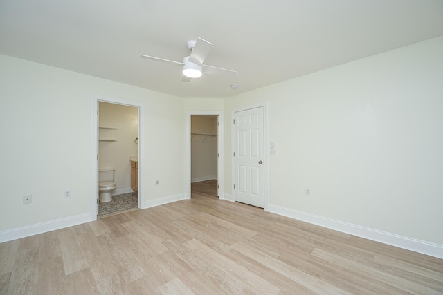 unfurnished bedroom with a closet, baseboards, a walk in closet, light wood-type flooring, and ensuite bath
