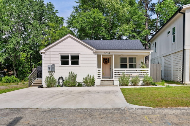 view of front of house with covered porch, roof with shingles, and a front yard