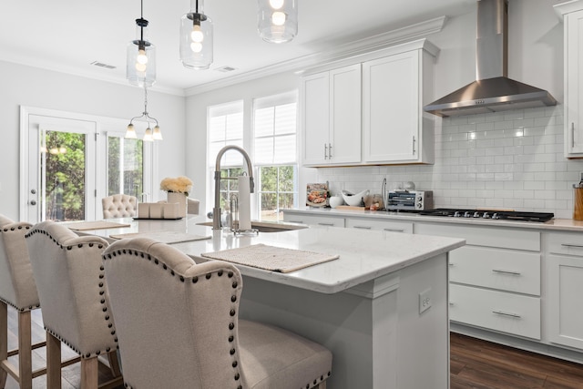 kitchen with visible vents, an island with sink, ornamental molding, dark wood-style floors, and wall chimney exhaust hood