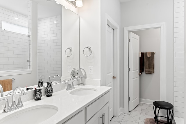 full bath with double vanity, baseboards, marble finish floor, and a sink