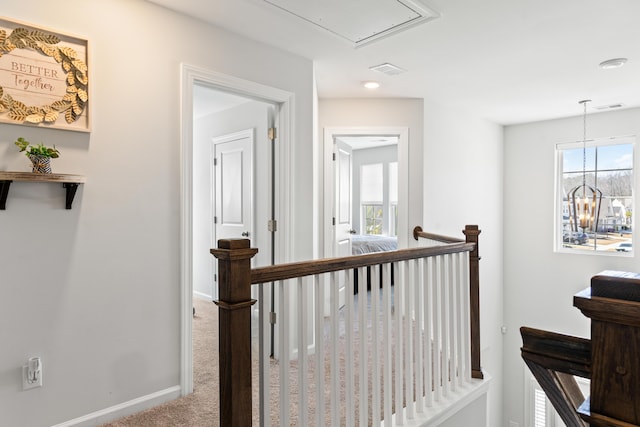 hallway featuring an upstairs landing, a notable chandelier, carpet floors, baseboards, and attic access