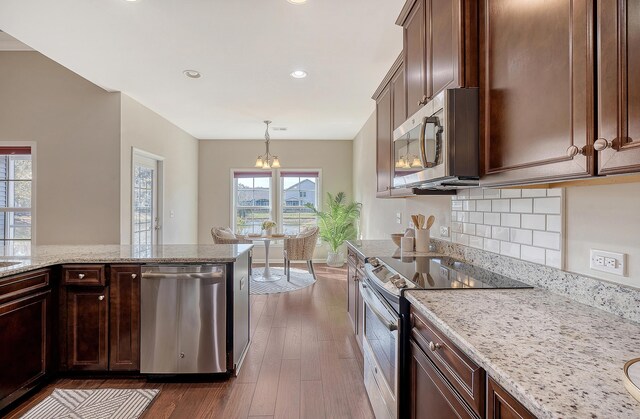 kitchen featuring dark wood-type flooring, hanging light fixtures, light stone countertops, stainless steel appliances, and a chandelier