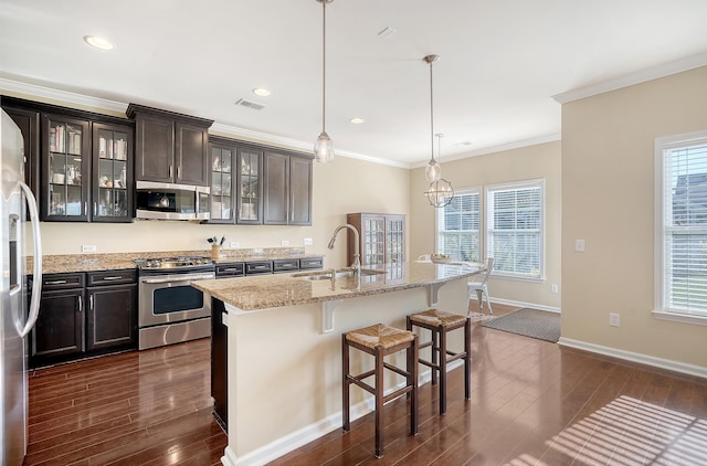 kitchen with appliances with stainless steel finishes, pendant lighting, dark brown cabinets, a kitchen island with sink, and sink