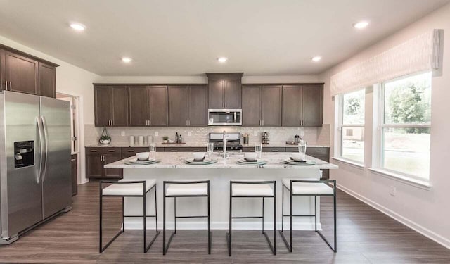 kitchen featuring dark brown cabinets, stainless steel appliances, an island with sink, and a kitchen bar