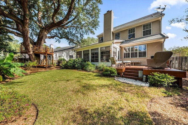 rear view of house featuring a wooden deck, a lawn, and a sunroom