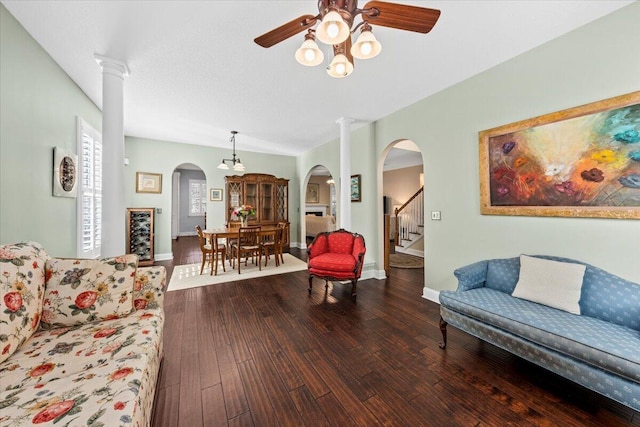 living room featuring ceiling fan, ornate columns, and dark wood-type flooring