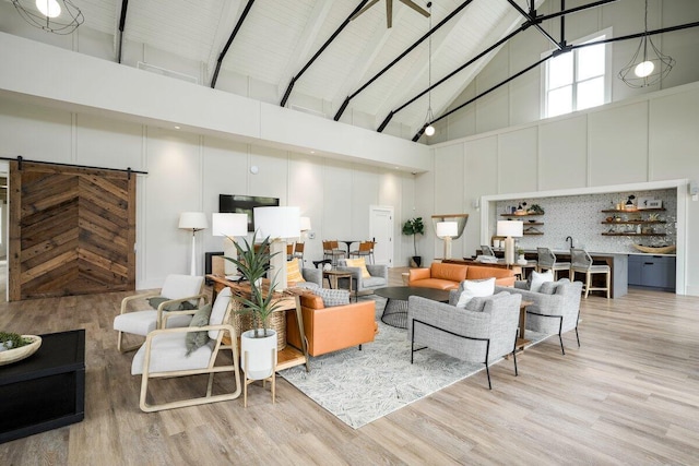 living room with a barn door, beam ceiling, a high ceiling, and light wood-type flooring