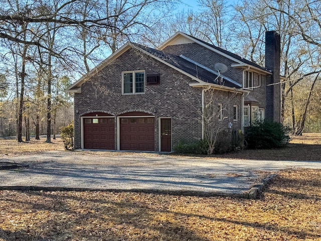 view of front of house featuring an attached garage, brick siding, a chimney, and gravel driveway