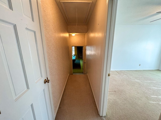 hall with attic access, light carpet, a textured wall, and baseboards