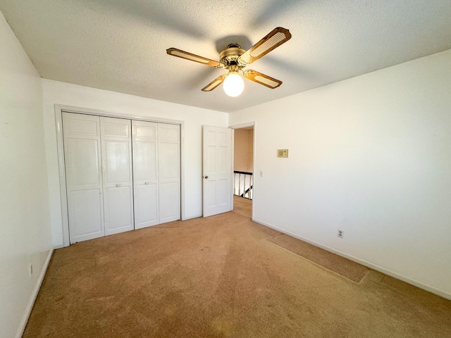 unfurnished bedroom with ceiling fan, a closet, a textured ceiling, and light colored carpet