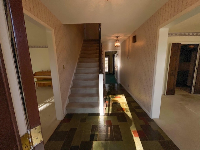 hallway featuring baseboards, stairway, and wallpapered walls