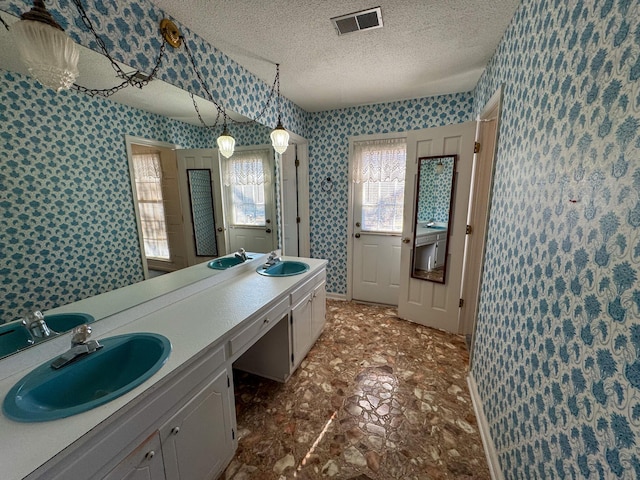 full bathroom with a textured ceiling, a sink, visible vents, and wallpapered walls