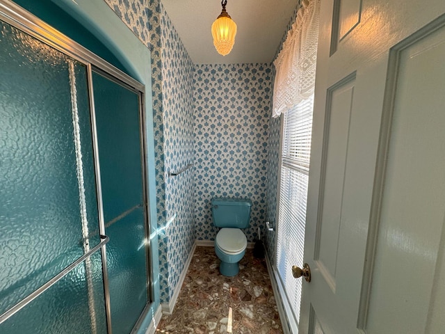 full bath with toilet, wallpapered walls, a shower stall, and baseboards