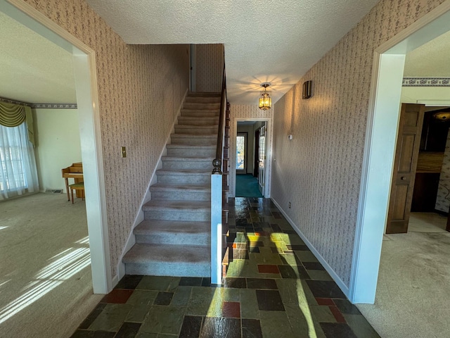 staircase featuring a textured ceiling, carpet floors, baseboards, and wallpapered walls