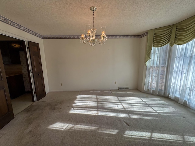 carpeted empty room featuring visible vents, a chandelier, and a textured ceiling