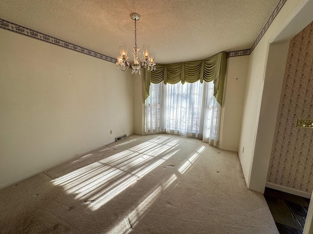 unfurnished room featuring a textured ceiling, visible vents, a notable chandelier, and light colored carpet