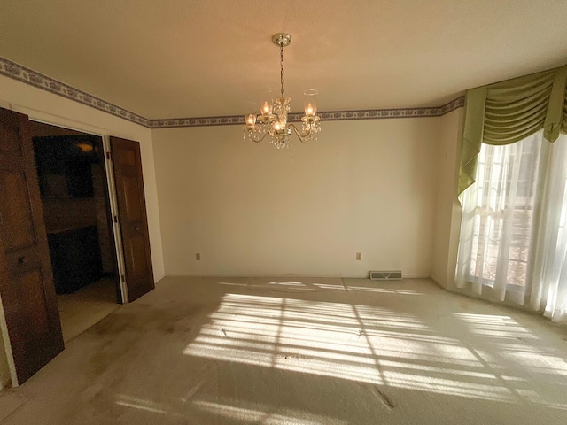 carpeted spare room featuring visible vents and a notable chandelier