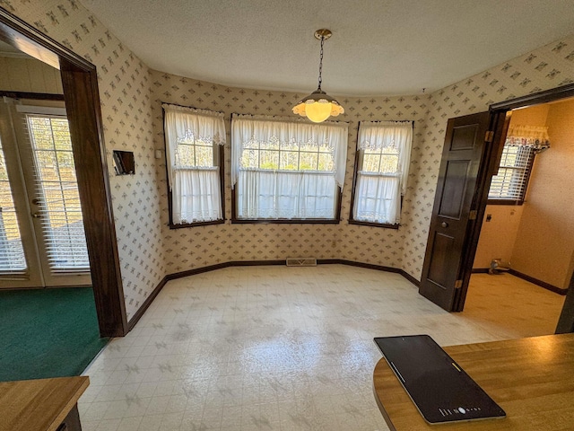 unfurnished dining area with a textured ceiling, baseboards, and wallpapered walls