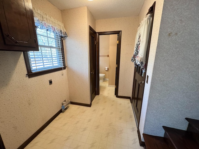 corridor with a textured ceiling, light floors, baseboards, and wallpapered walls