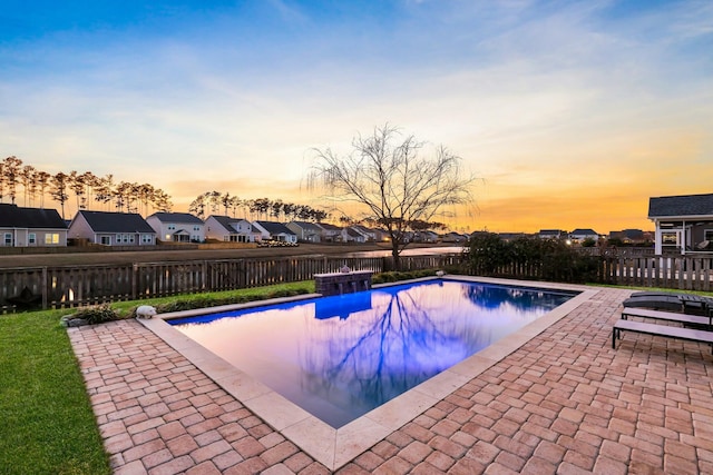 pool at dusk with a fenced in pool, a residential view, a fenced backyard, and a patio