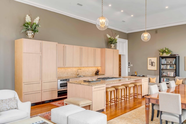 kitchen with light brown cabinetry, pendant lighting, and light stone countertops