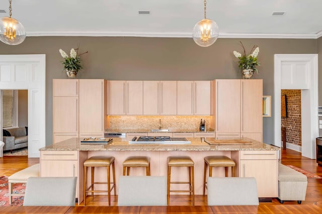 kitchen with light brown cabinets, a kitchen island with sink, and decorative light fixtures