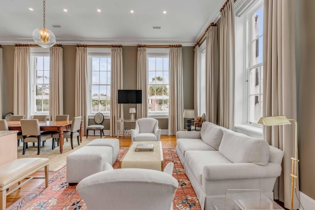 living area with a wealth of natural light, visible vents, crown molding, and light wood finished floors