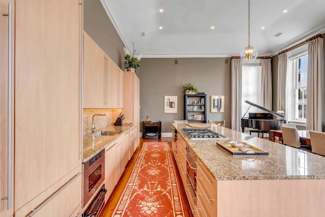 kitchen with light brown cabinets, a sink, a kitchen island, light stone countertops, and pendant lighting