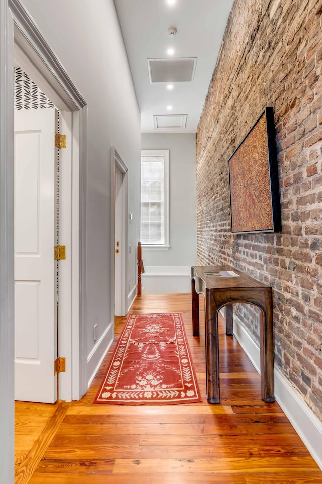 hall with baseboards, brick wall, attic access, and wood finished floors