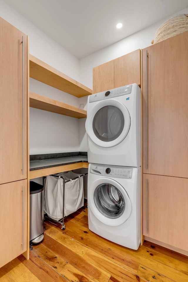 laundry room with stacked washer / drying machine, cabinet space, and light wood finished floors