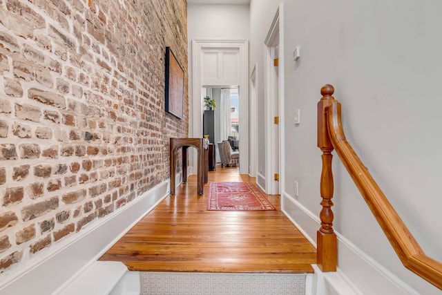 hall with brick wall, wood finished floors, and baseboards