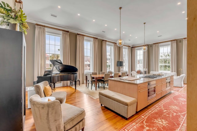 kitchen with visible vents, a kitchen island, crown molding, light brown cabinetry, and stainless steel oven