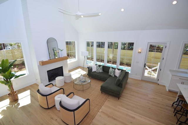 living room with baseboards, ceiling fan, a fireplace, light wood-style floors, and high vaulted ceiling