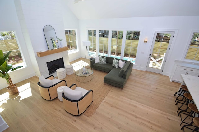 living area featuring baseboards, vaulted ceiling, a fireplace, and light wood finished floors