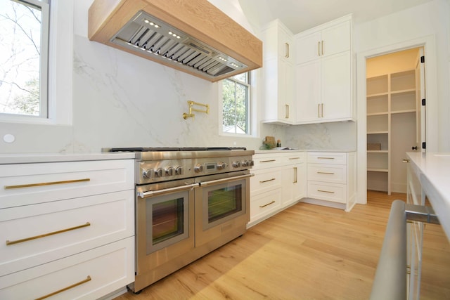 kitchen featuring range with two ovens, decorative backsplash, light wood-style floors, and custom exhaust hood