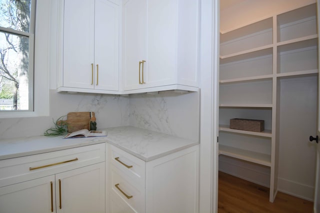 interior space with light stone counters, wood finished floors, backsplash, and white cabinets