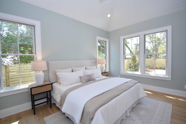 bedroom with lofted ceiling, multiple windows, wood finished floors, and baseboards