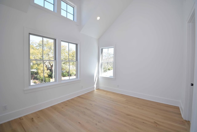 spare room featuring a towering ceiling, recessed lighting, baseboards, and light wood finished floors